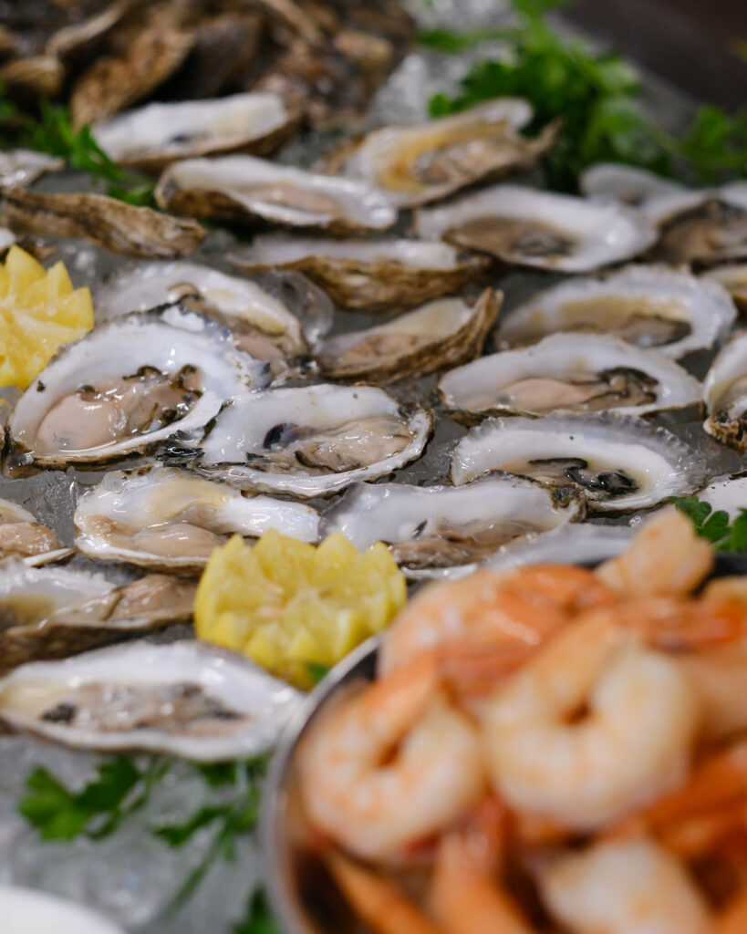 Overhead shot of raw oysters on crushed ice with lemon wedges and edible flowers at a luxury catering station.